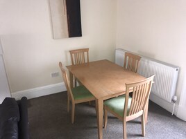A dining area with a wooden table and four chairs, a radiator, and a black object on the floor.