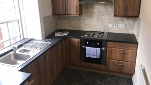 Eine kompakte Küche mit Holzausstattung, einem Gasherd, einem Geschirrspüler und einer gefliesten Spritzschutzwand.