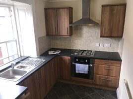 Una cocina compacta con armarios de madera, estufa a gas, lavavajillas y salpicadero de azulejos.