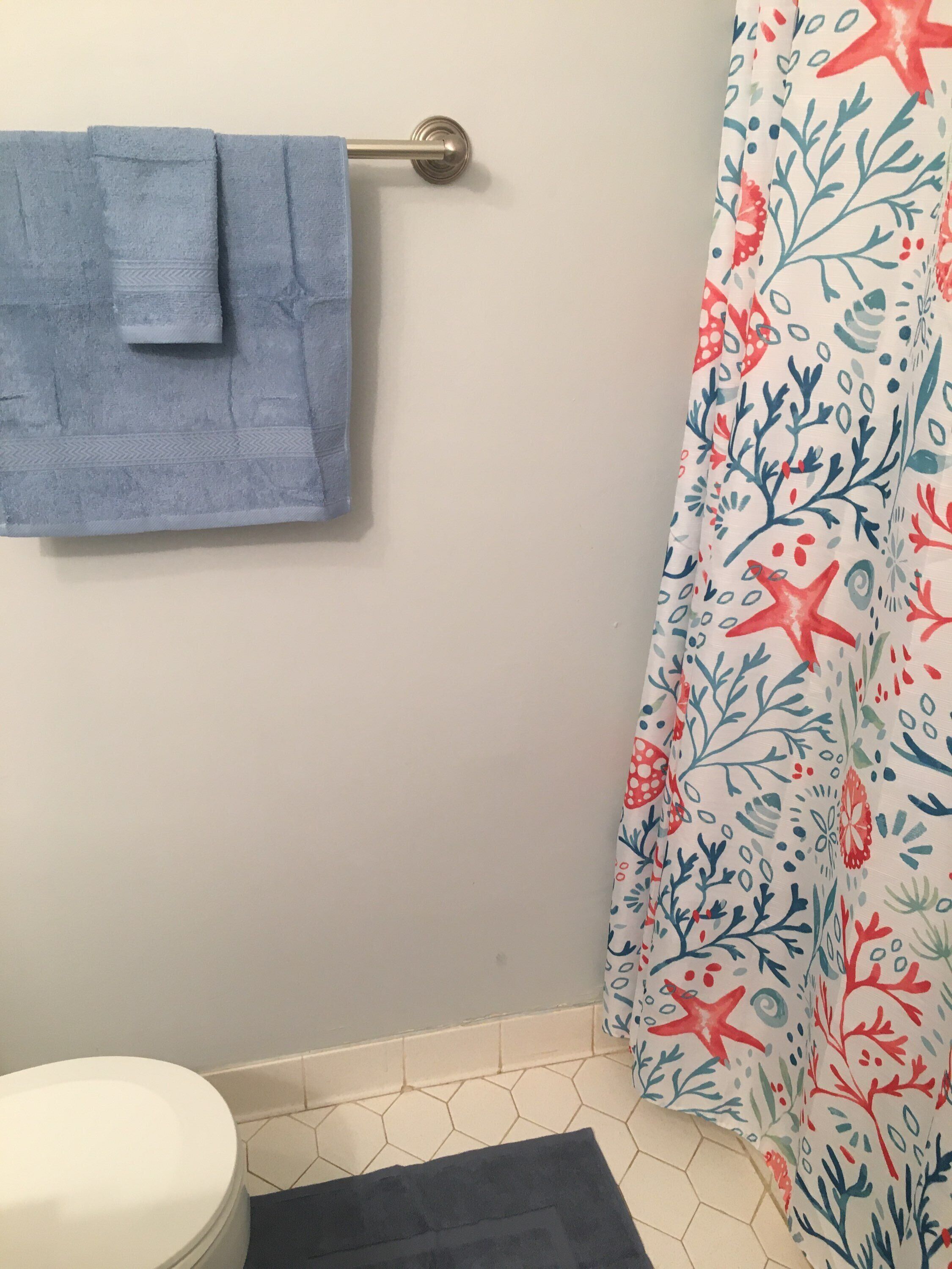 A bathroom with a blue towel hanging on a metal towel bar, a white toilet, and a shower curtain with a marine-themed pattern.