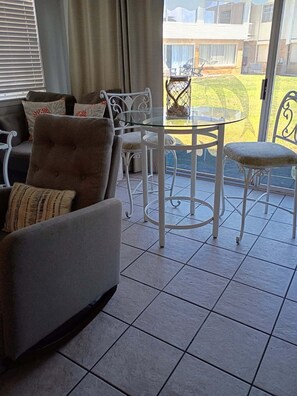 A furnished living area with a sofa, chairs, a glass-top table, and a view of a building through a window.