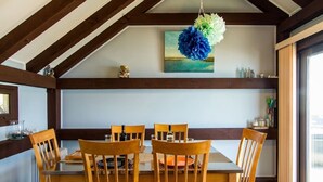 A dining area with a wooden table and chairs, a hanging decorative piece, and a painting on the wall.
