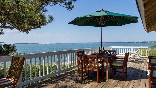 A wooden deck with a table and chairs, an umbrella, and a view of the sea.