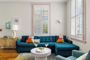 A living room with a teal sectional sofa, a round coffee table, and a wooden cabinet. - Vibrant Charm & Dining Pleasures | The Hurricane (Charleston)