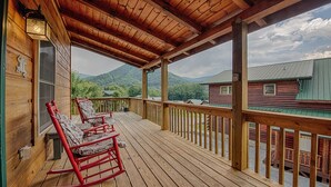 Une terrasse en bois avec deux fauteuils à bascule et une vue sur une montagne et un chalet.