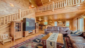 Un intérieur de cabane en bois spacieux, comprenant un espace de vie, un téléviseur, un canapé et un escalier.