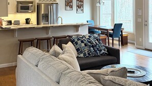 Eine moderne Küche mit Edelstahlgeräten, eine Essecke mit einem blauen Stuhl und ein Wohnzimmer mit einem grauen Sofa.