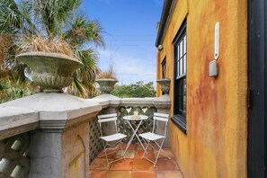 Pequeño patio al aire libre con una mesa y dos sillas, rodeado por una barandilla de piedra y una pared amarilla.