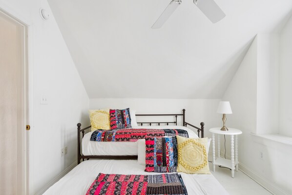 A bedroom with two beds, a white lamp, and a ceiling fan.