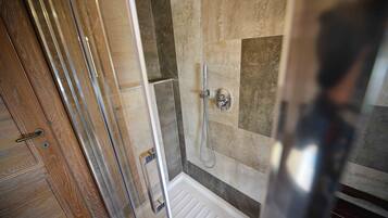 A shower area with a glass door, a showerhead, and a tiled wall.
