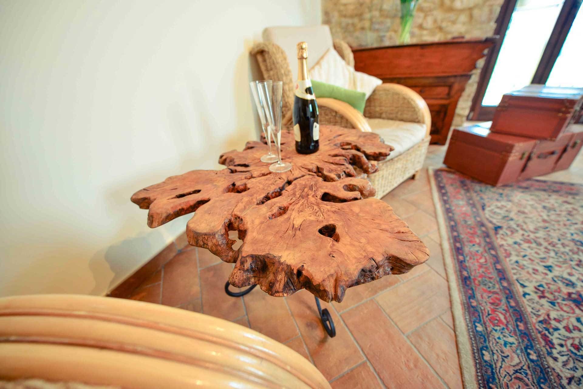 Una mesa de centro de madera con un diseño único, una botella de champán y un florero con flores en un salón.