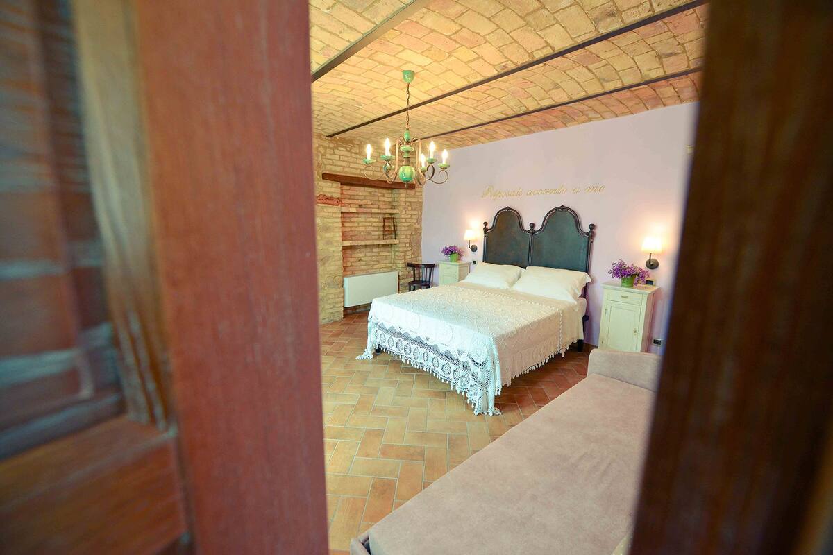 A bedroom with a large bed, a wooden headboard, a brick wall, and a chandelier.