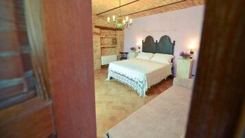 A bedroom with a large bed, a wooden headboard, a brick wall, and a chandelier.