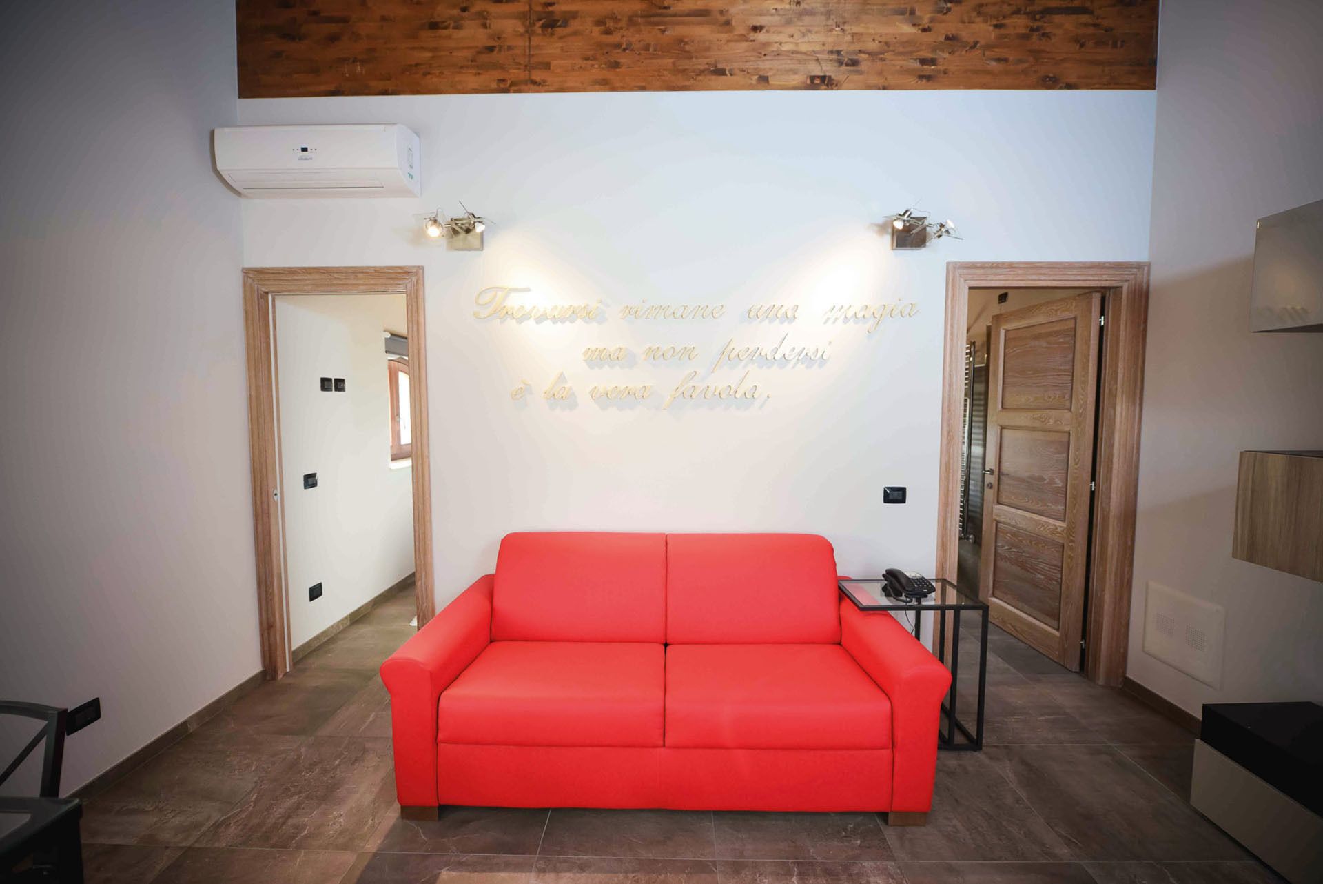 Una sala de estar moderna con un sofá rojo, un aire acondicionado instalado en la pared y una lámpara decorativa.
