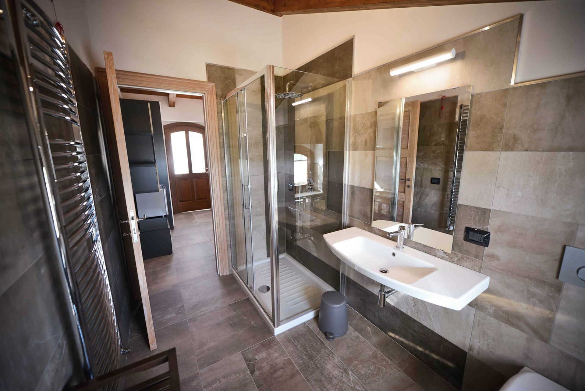 Une salle de bain moderne avec une douche à l’italienne en verre, un lavabo blanc et un grand miroir.