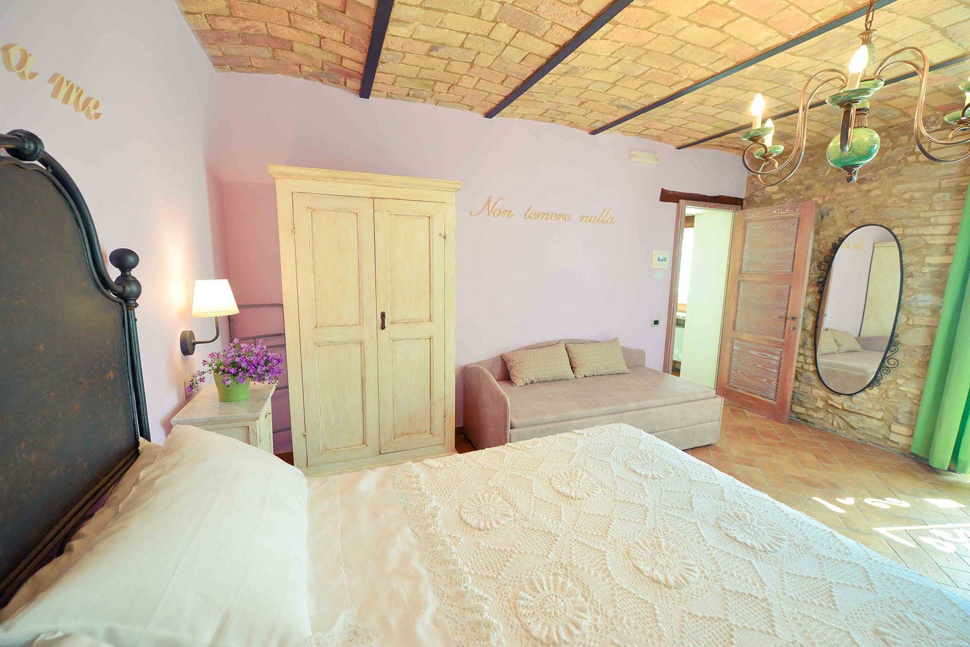 Un dormitorio con cama, armario, sofá, espejo y candelabro.
