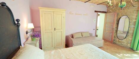 A bedroom with a bed, a wardrobe, a sofa, a mirror, and a chandelier.