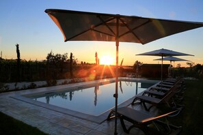 A swimming pool with lounge chairs and umbrellas, surrounded by a garden and a view of the sunset. - Casale905 (Crecchio)