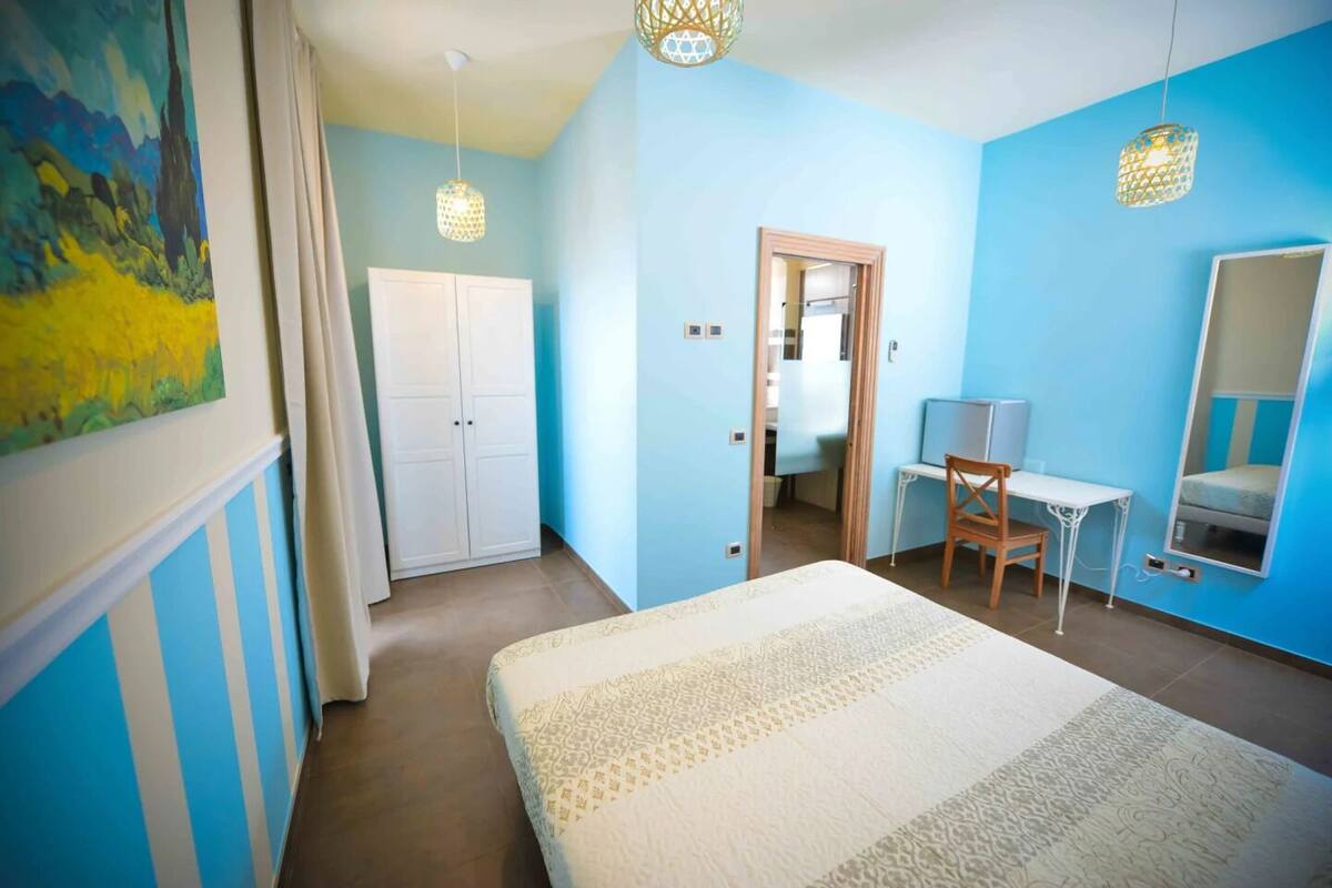 A bedroom with a bed, a desk, a chair, a wardrobe, and a mirror.