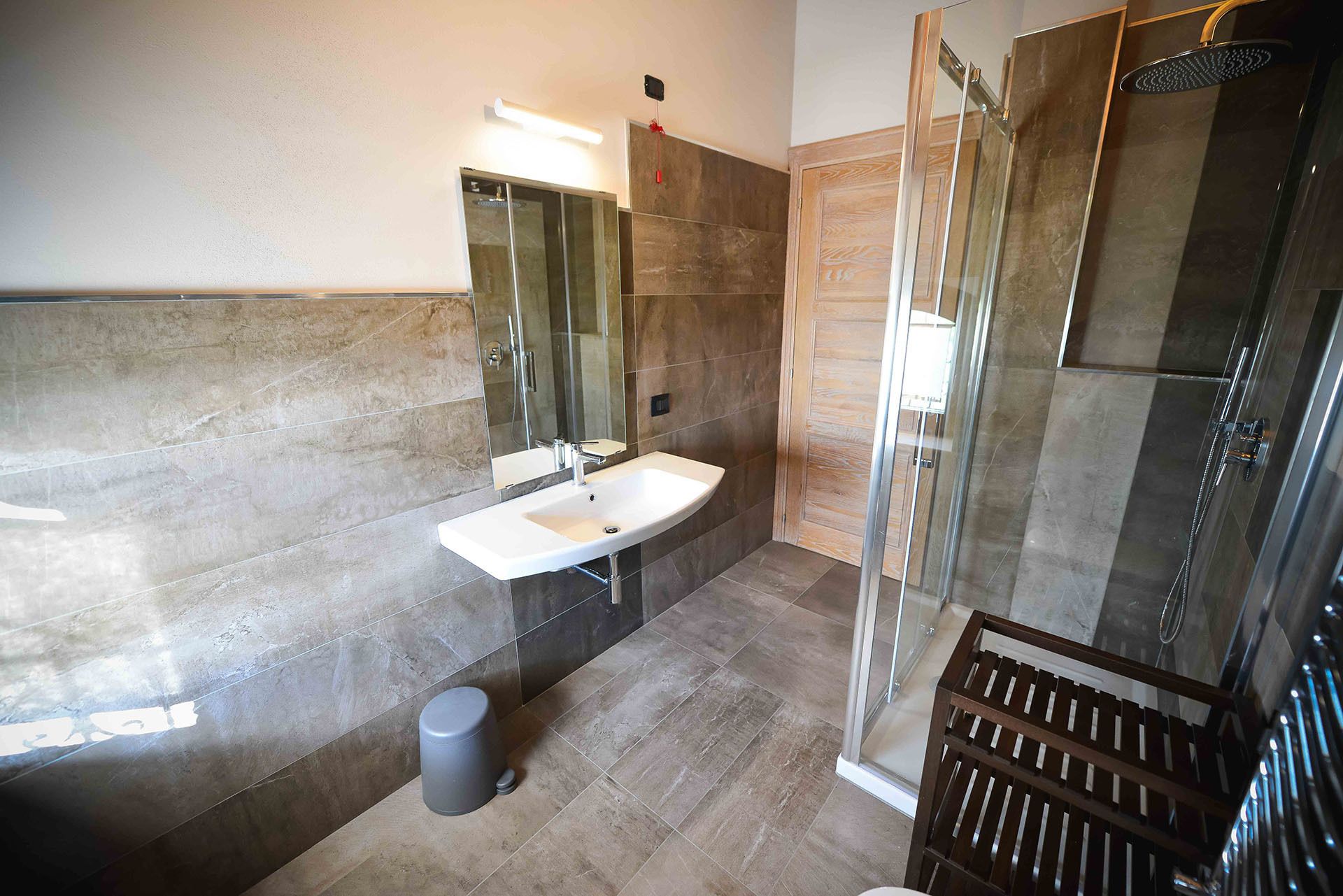Une salle de bain moderne avec une douche à parois de verre, un lavabo avec un miroir et une poubelle.