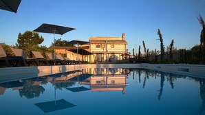 Una piscina con sillas de descanso y sombrillas, un edificio grande con tejado de baldosas y un cielo despejado.
