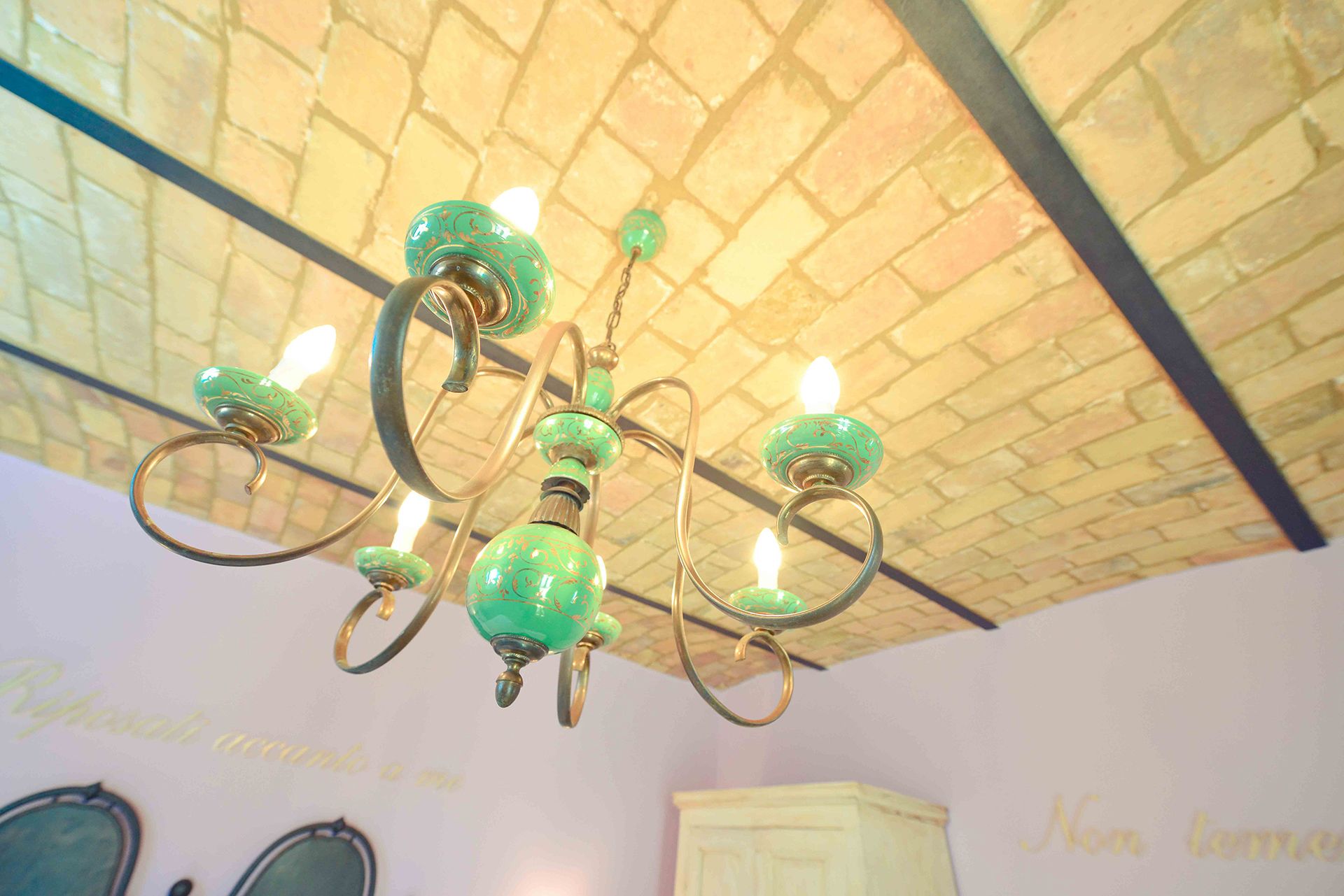 Un lustre doté d’abat-jours en verre vert et de fixations en laiton, dans une pièce dont le plafond est recouvert de carreaux et qui contient un meuble blanc.