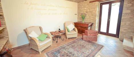 A cozy living room with two wicker chairs, a small table with a bottle, a rug, and a stone wall with a quote.