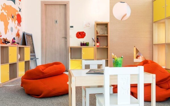 Un cuarto de juegos infantil con una mesa de madera, sillones de saco naranja y unidades de almacenamiento de colores.