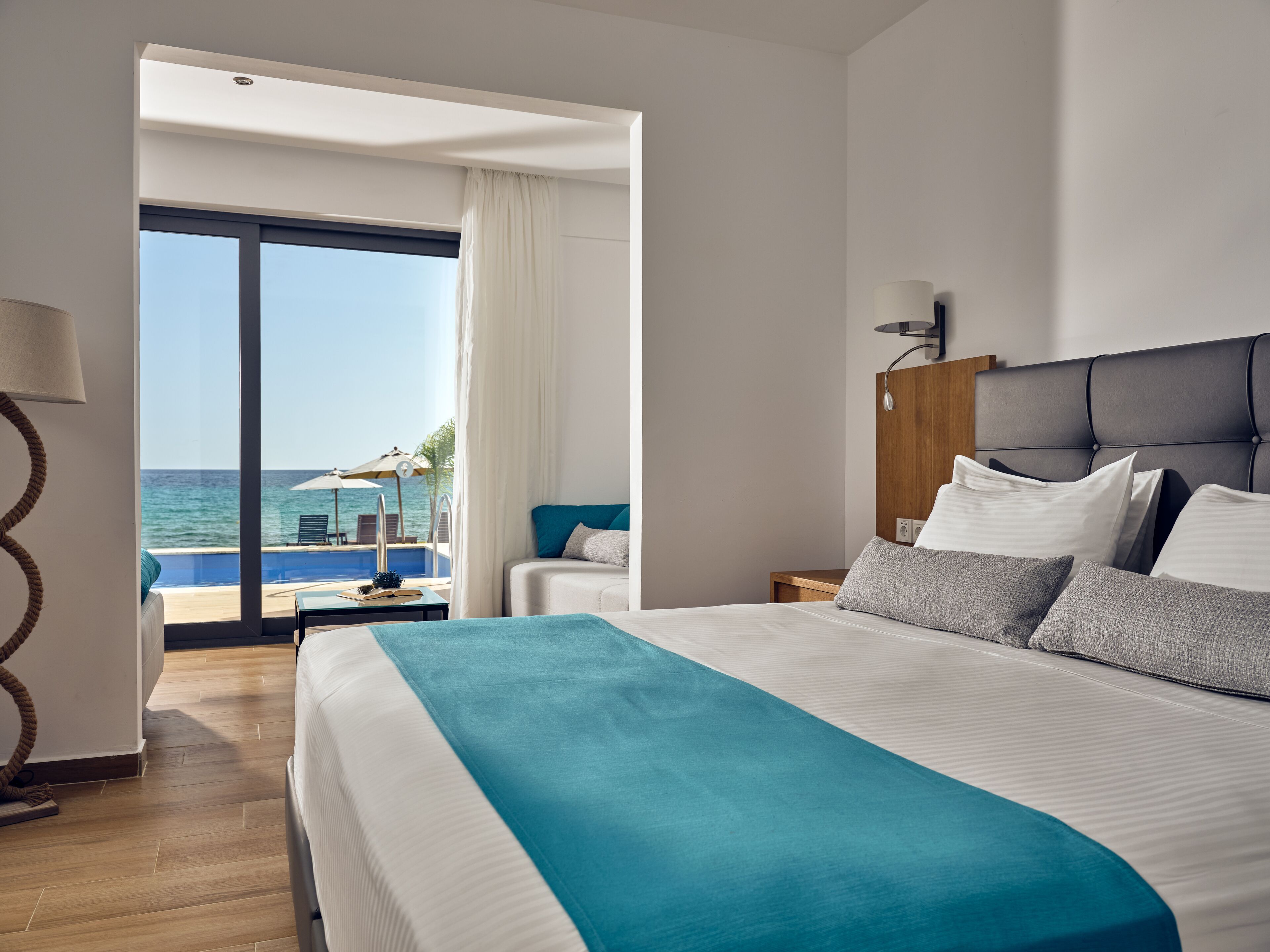 Une chambre d’hôtel avec un grand lit, une vue sur la mer, un plancher en bois et une table de chevet avec une lampe.