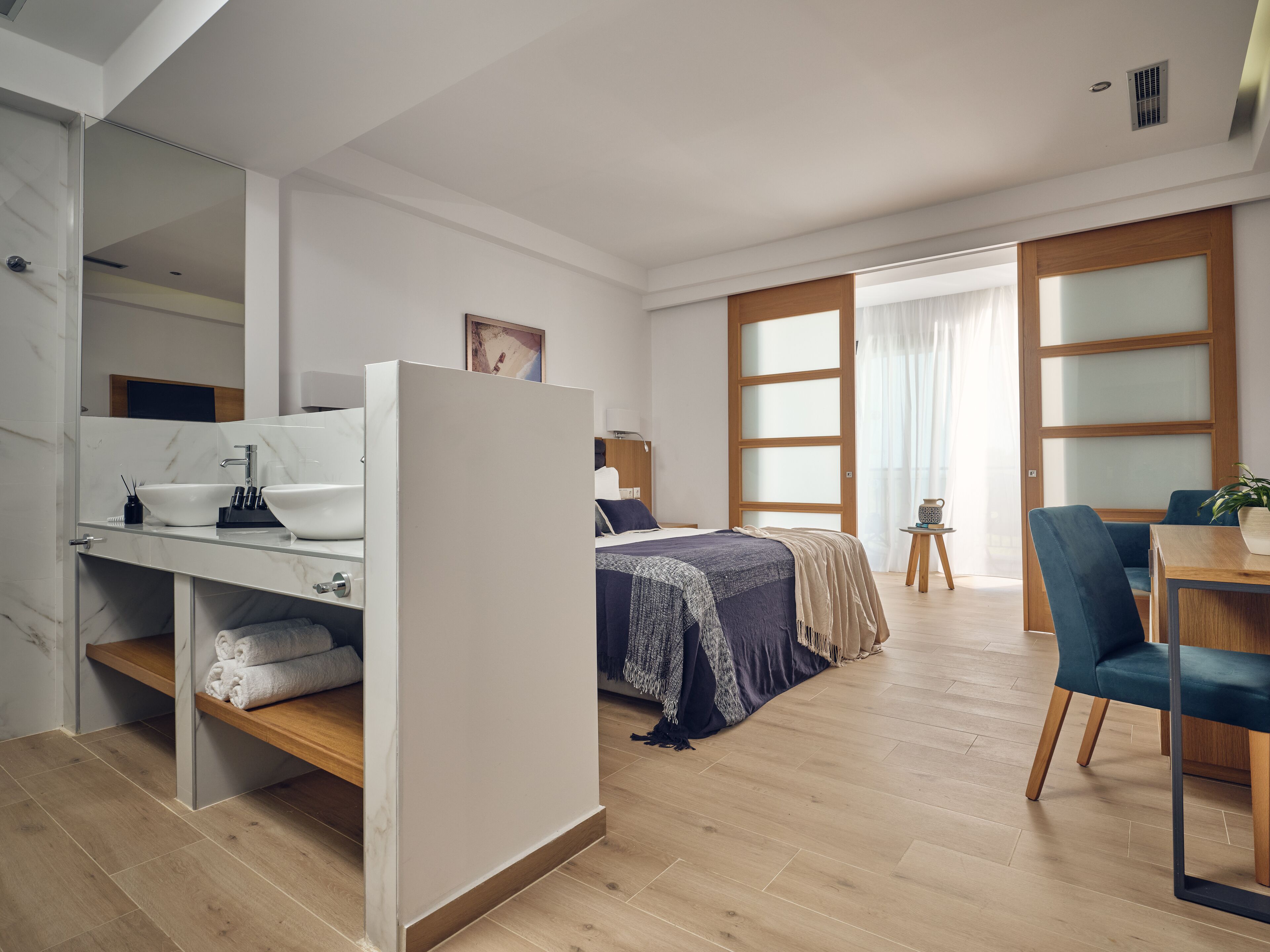 A modern bedroom with a bed, a desk with a mirror, a small table, and a chair.