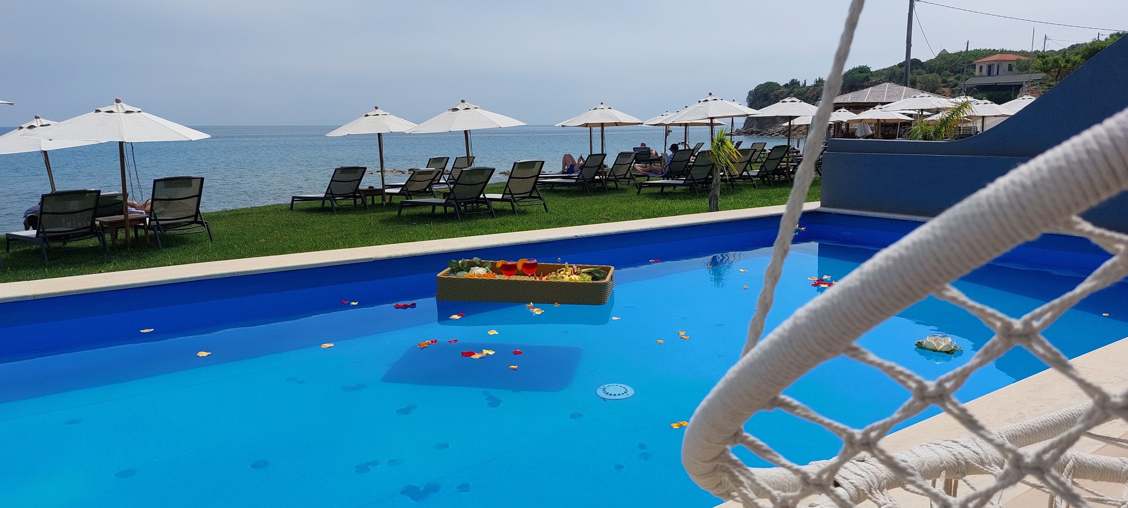 A pool with lounge chairs and umbrellas, a rope barrier, and a view of the sea.
