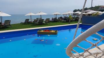 A pool with lounge chairs and umbrellas, a rope barrier, and a view of the sea.