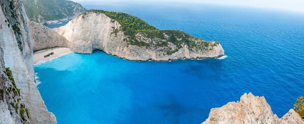 A coastal cliff with a narrow beach and a boat anchored near the shore. - Cavo Orient Beach Hotel (Zakynthos)
