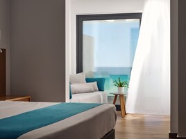 Una camera da letto moderna con un letto grande, un tavolino con una pianta e vista sull'oceano da una finestra ampia.