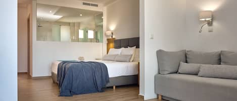 A modern bedroom with a bed, a sofa, a mirror, and a wall-mounted lamp.