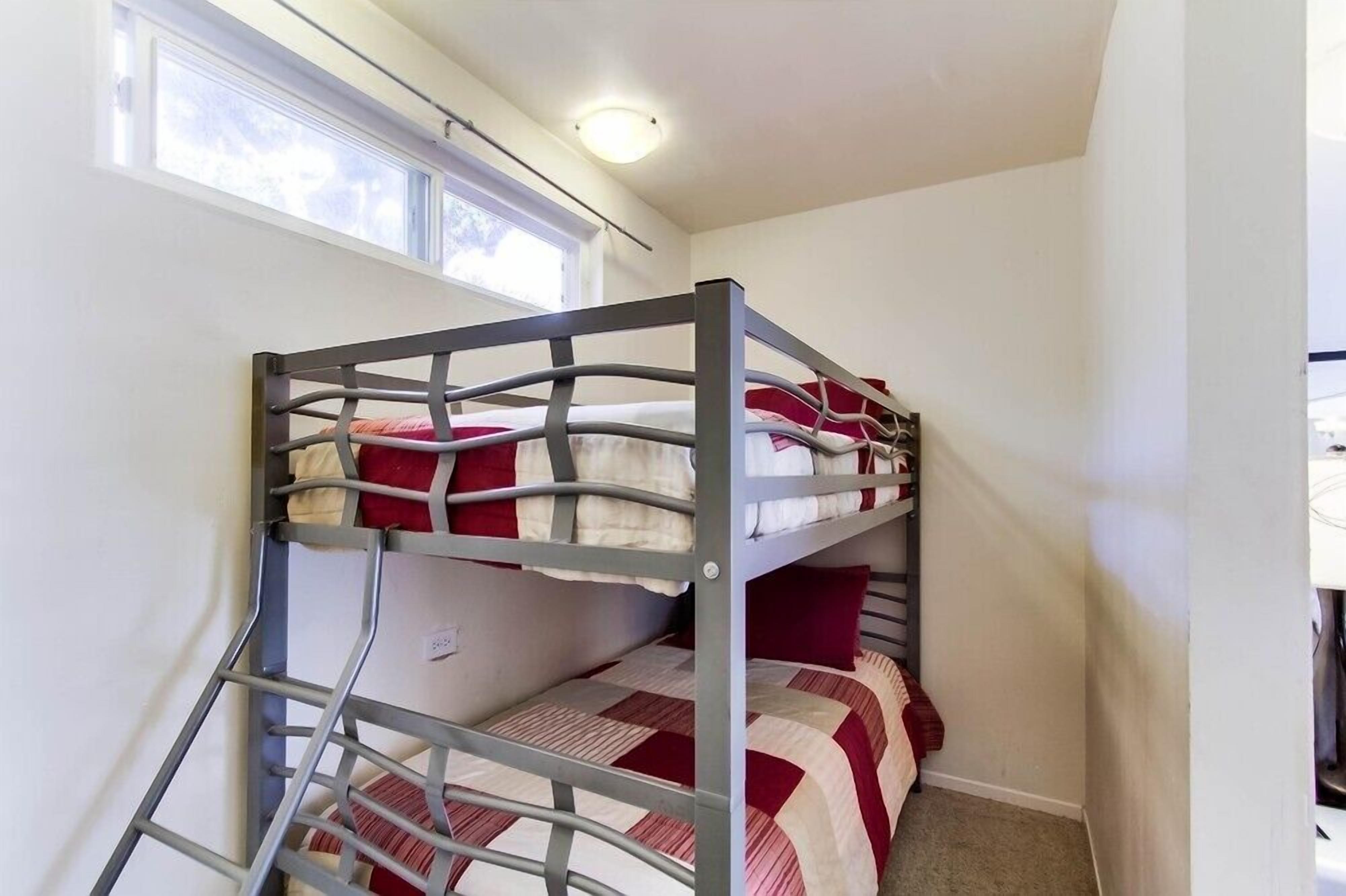 Un lit superposé avec une échelle, des murs blancs et une fenêtre.