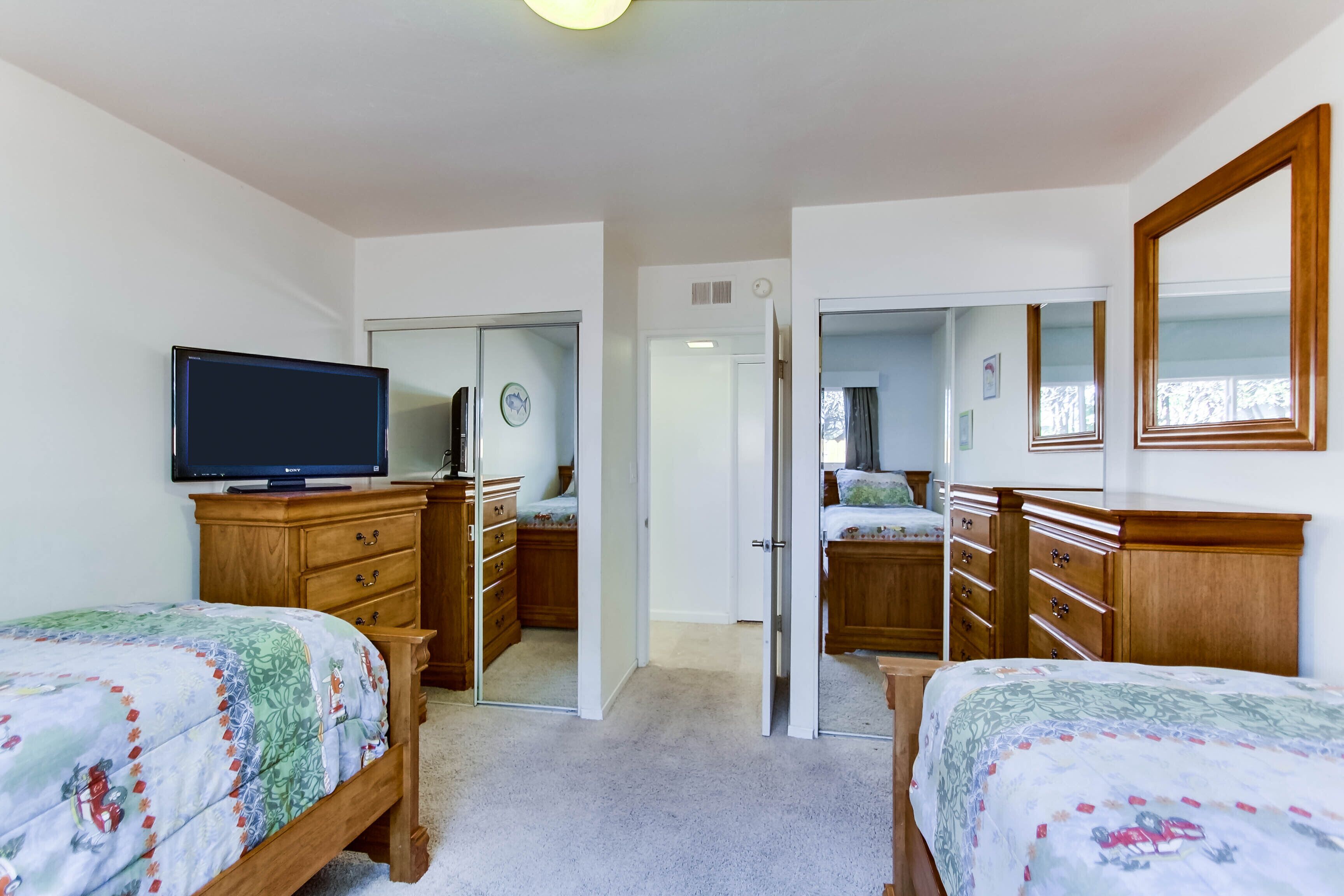 A bedroom with two beds, a television, wooden furniture, and a mirror.