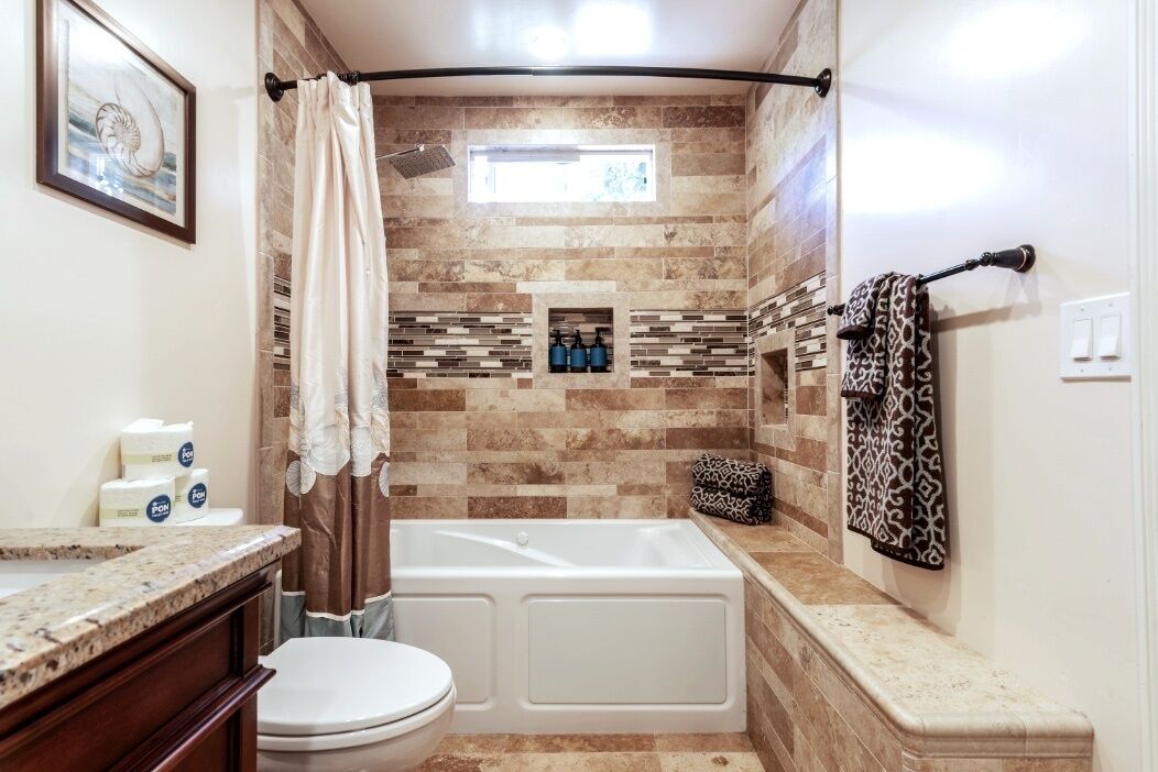 Une salle de bain avec une baignoire, des toilettes et un rideau de douche. On y trouve des articles de toilette sur le comptoir et un porte-serviettes avec des serviettes à motifs.