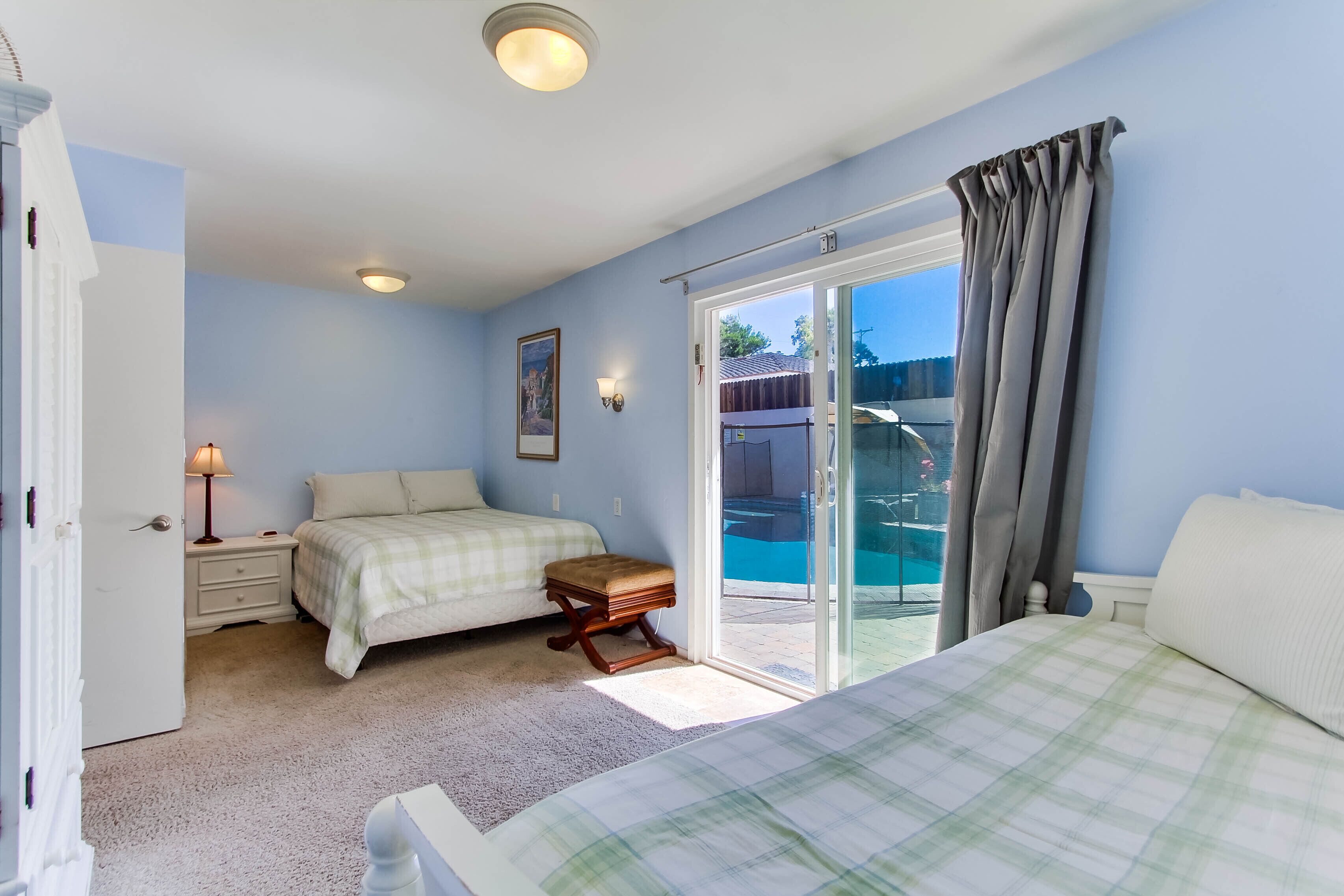 Une chambre avec deux lits, une table de chevet, une lampe et une porte-fenêtre coulissante donnant sur une piscine.