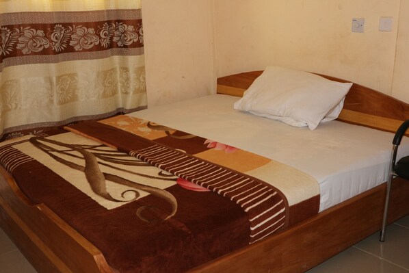Una cama individual con cabecera de madera, almohada blanca y manta marrón y beige estampada.