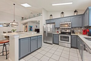 A modern kitchen with grey cabinets, stainless steel appliances, and a marble countertop. - Disney Magic 3 Miles Away! 5BR Villa w/ Heated Pool, Custom Murals & Game Room (Kissimmee)