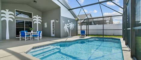 Una piscina interior con techo de cristal, sillas azules y un mural de palmeras.