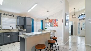 A modern kitchen with dark cabinets, a marble island, and bar stools. - Unique Disney Villa 5BR, Heated pool, Hand-Painted Murals, 3 Miles to Disney (Kissimmee)