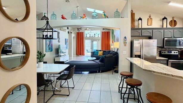 A modern kitchen with a dining area, a living room with a sofa, and a visible ceiling light fixture. - Unique Disney Villa 5BR, Heated pool, Hand-Painted Murals, 3 Miles to Disney (Kissimmee)