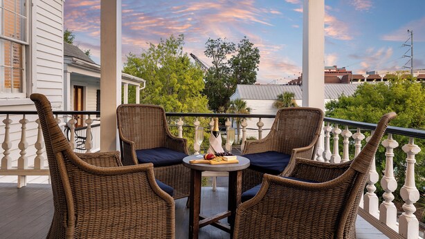 A balcony with wicker chairs and a table set with a bottle, grapes, and a fruit.