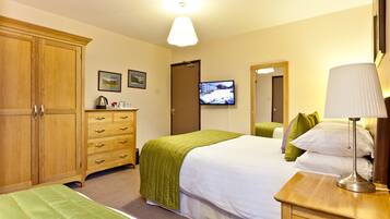 Een hotelkamer met een grote houten garderobe, een bed met groen beddengoed, een nachtkastje met een lamp en een televisie aan de muur.