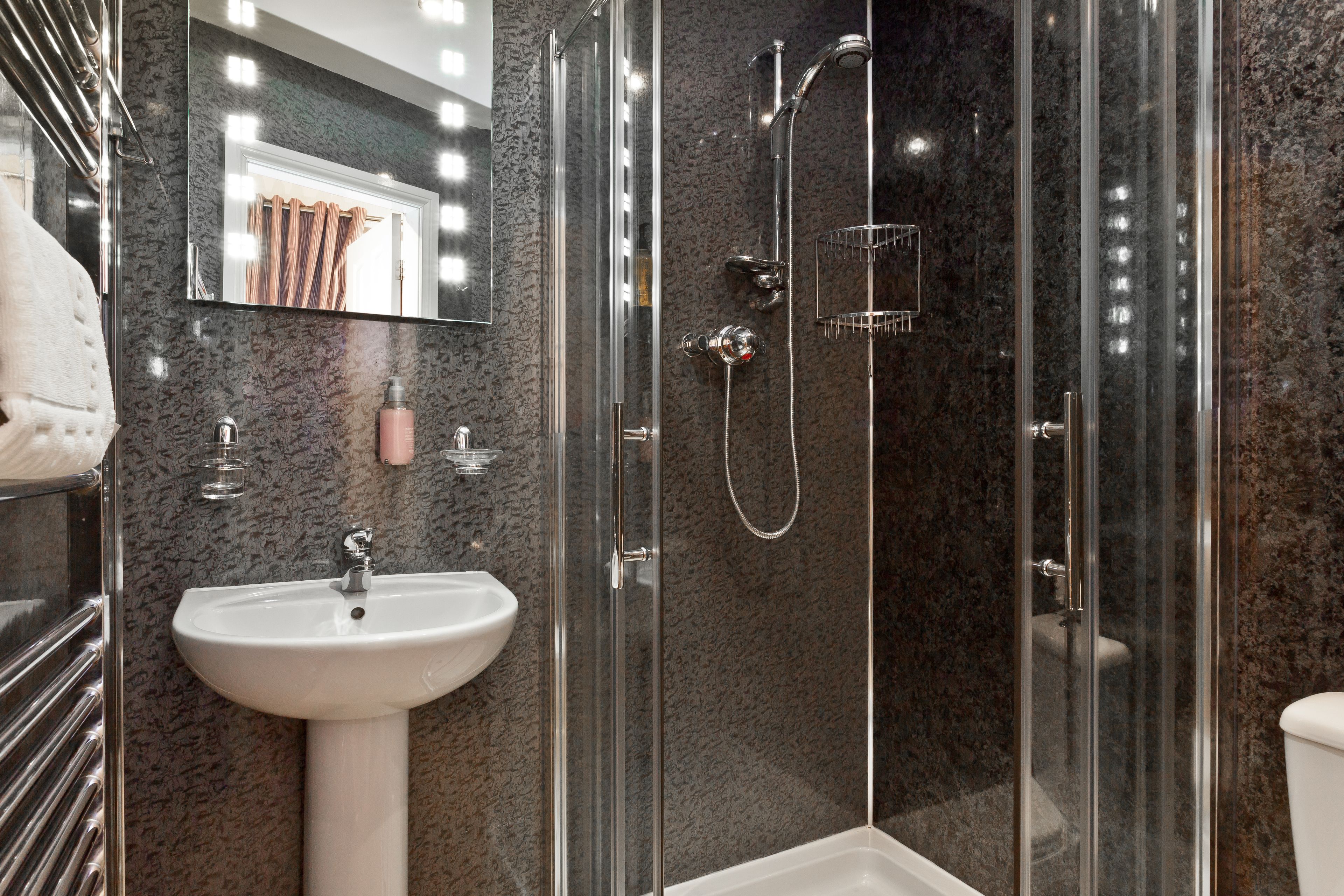 A modern bathroom with a glass-enclosed shower, a white pedestal sink, and a large mirror with lights.