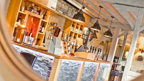 A bar area with wooden shelves stocked with bottles, a cash register, and hanging pendant lights.