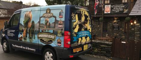 Una camioneta de reparto con la marca de Windermere Brewing Company, estacionada cerca de un pub llamado The Watermill Inn & Brewery.
