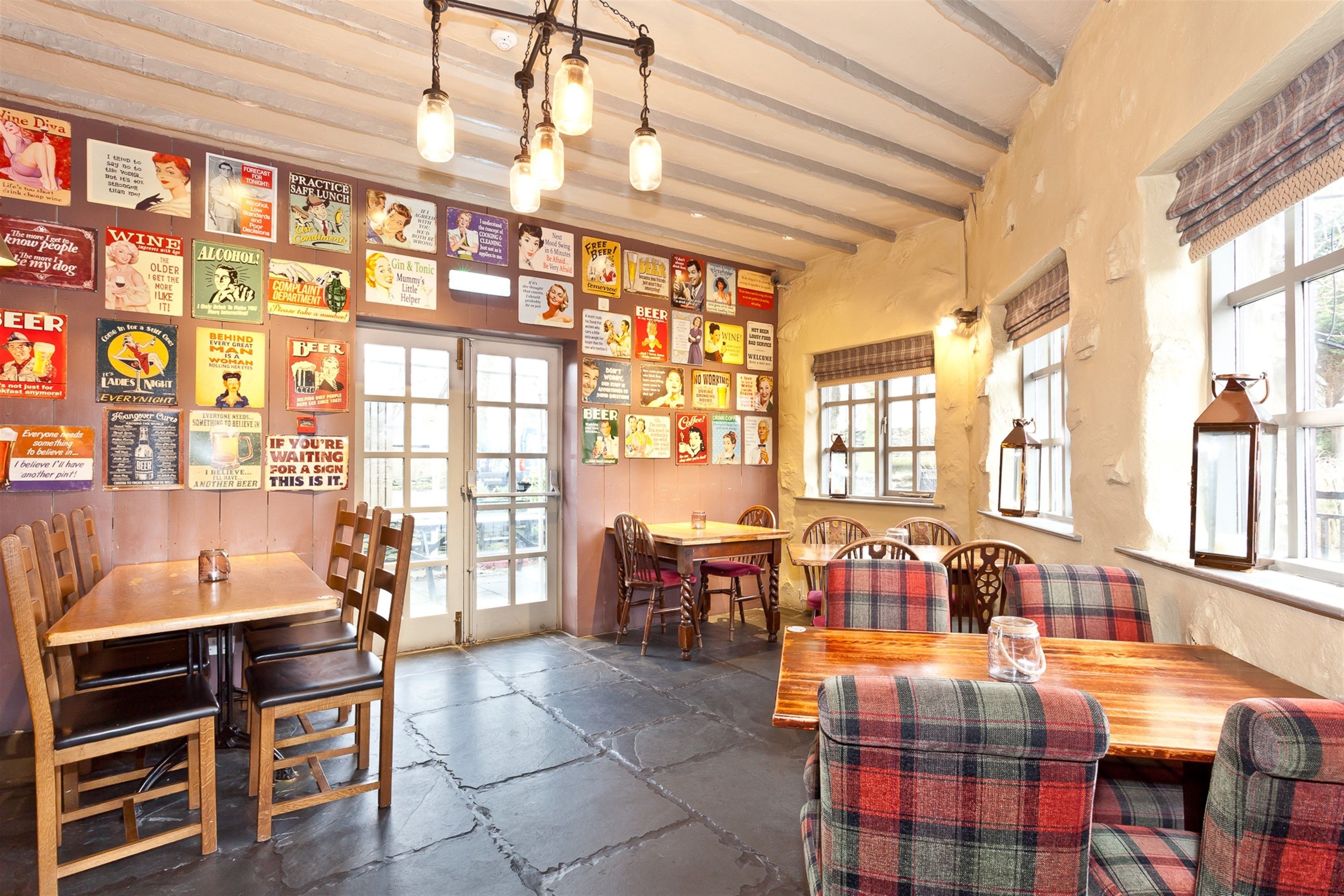 A restaurant interior with wooden tables and chairs, posters on the walls, and large windows.